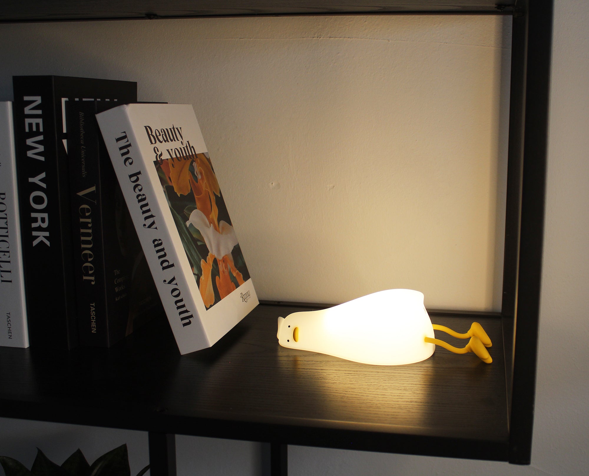 Lampada da notte Winkee Duck accesa su una mensola