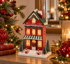 Diorama Casetta Natalizia LED EDG Enzo De Gasperi Exclusive ambientata su un mobile con albero di Natale, decorazioni rosse e luci calde, per un'atmosfera natalizia accogliente.