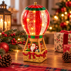 Mongolfiera natalizia EDG H25 cm con Babbo Natale nella cesta, effetto glitter e luci LED, ambientata su una consolle con decorazioni natalizie e luci calde.