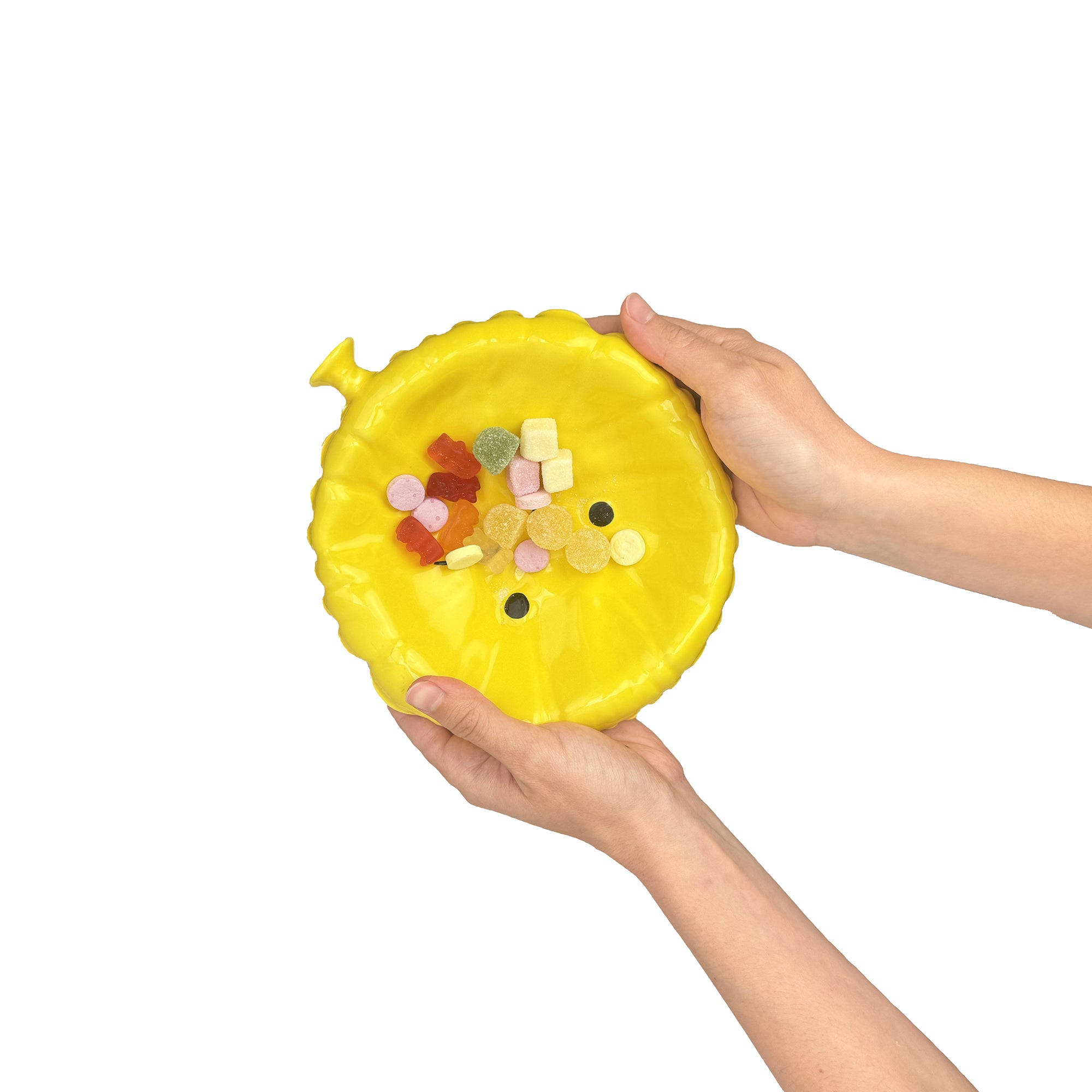 Vassoio Sad Balloon giallo in ceramica lucida sostenuto con due mani, vista dall'alto che mostra le proporzioni del portaoggetti di design con caramelle.
