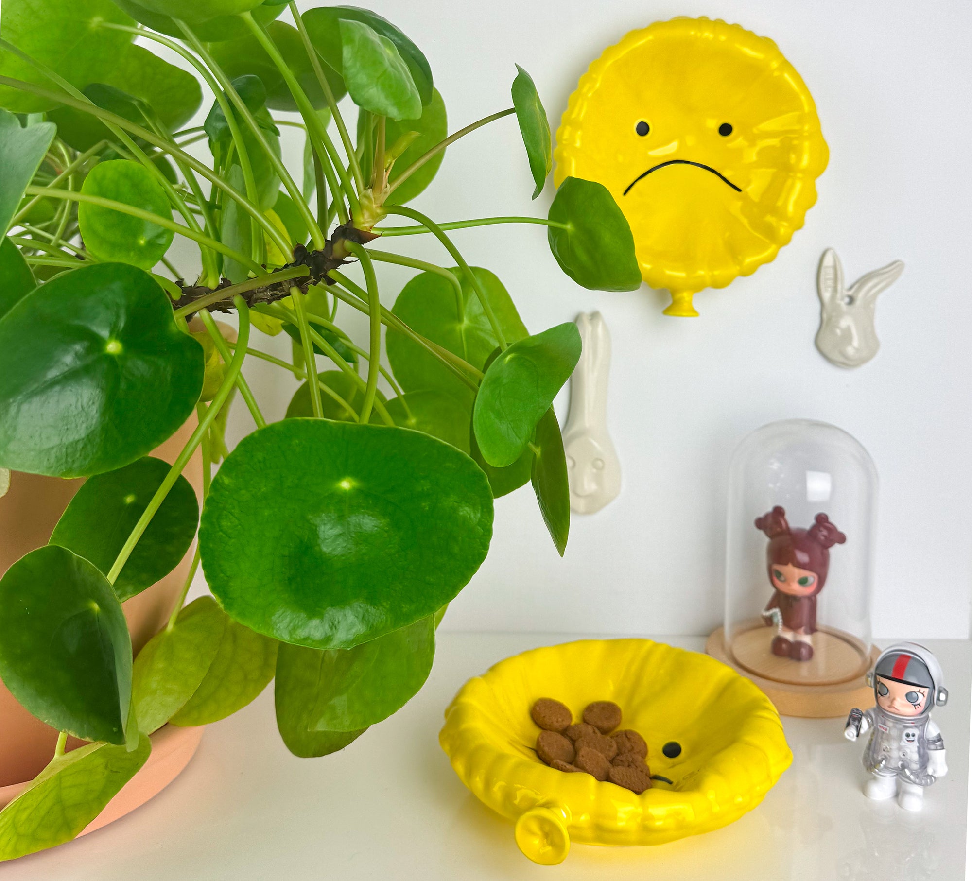 Portaoggetti Sad Balloon giallo in ceramica smaltata, ambientato con pianta verde e complementi decorativi, svuotatasche originale dal design ironico.